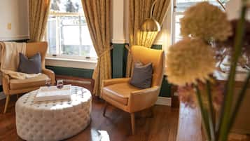 A room with two leather armchairs, a round ottoman, and a table with glasses of red wine.