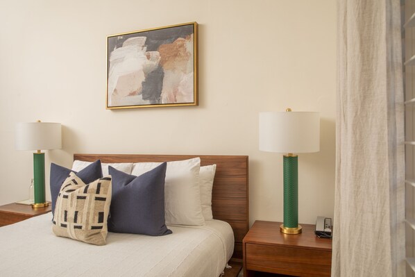 A neatly made bed with a wooden headboard, two bedside tables with lamps, and a framed abstract painting on the wall.