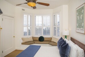 Ein Schlafzimmer mit einem großen Bett, einer Sitzbank unter dem Fenster mit einem grünen Kissen und einem Deckenventilator.