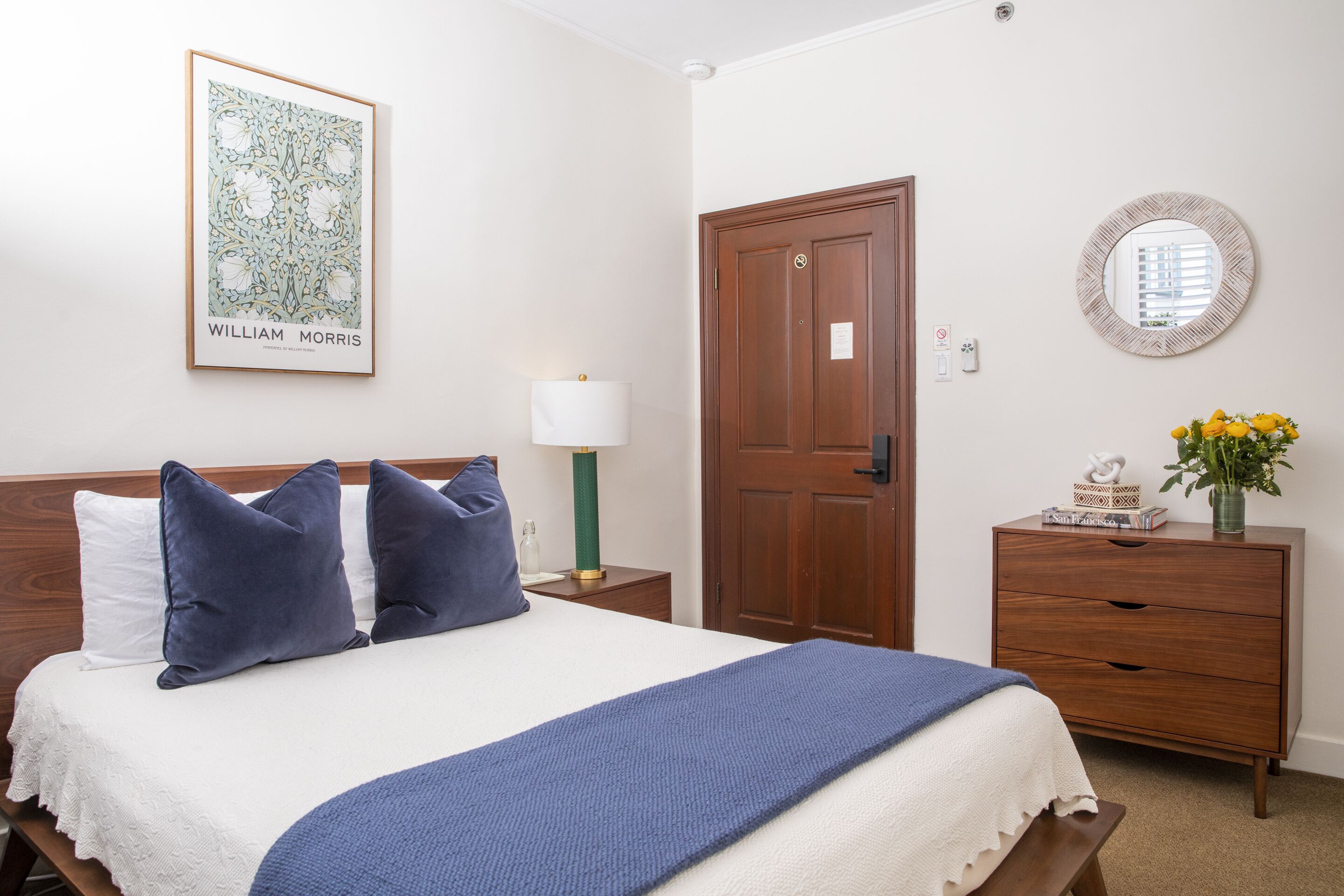 Une chambre à coucher bien rangée, avec un lit, des oreillers, une lampe de chevet, une commode et un tableau encadré au mur.