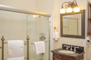 Une salle de bain dotée d’une douche à parois de verre, d’un lavabo avec un meuble-vasque en bois et d’un miroir orné d’un cadre décoratif.