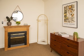 Une pièce avec une cheminée en bois, un miroir, un tableau encadré, une lampe sur pied et une commode en bois.