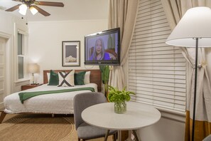 Une chambre d’hôtel avec un lit, une chaise, une petite table, un téléviseur et une fenêtre avec des stores.