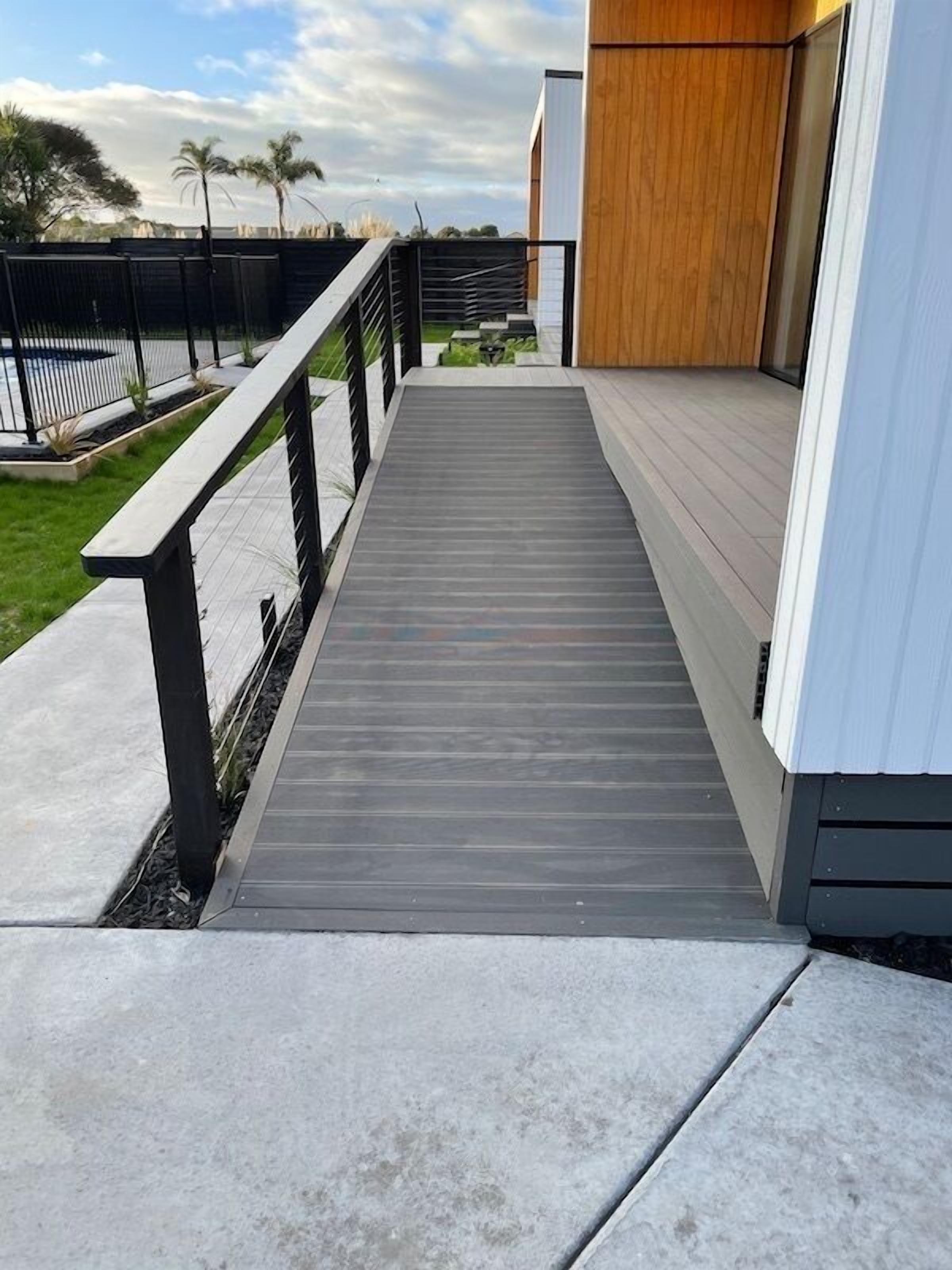 A wooden deck leading to a modern building with a white exterior and a wooden door.