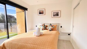 A bedroom with a large bed, two framed pictures on the wall, and a view of the outdoors through a sliding door. - Ohope Villas (Ohope)