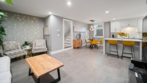 A modern living room with a sofa, a coffee table, and a staircase leading to a kitchen area with bar stools. - BOOK 7 NITES AND GET A DISCOUNT 2 BEDROOM PRIVATE UNIT (Portland)