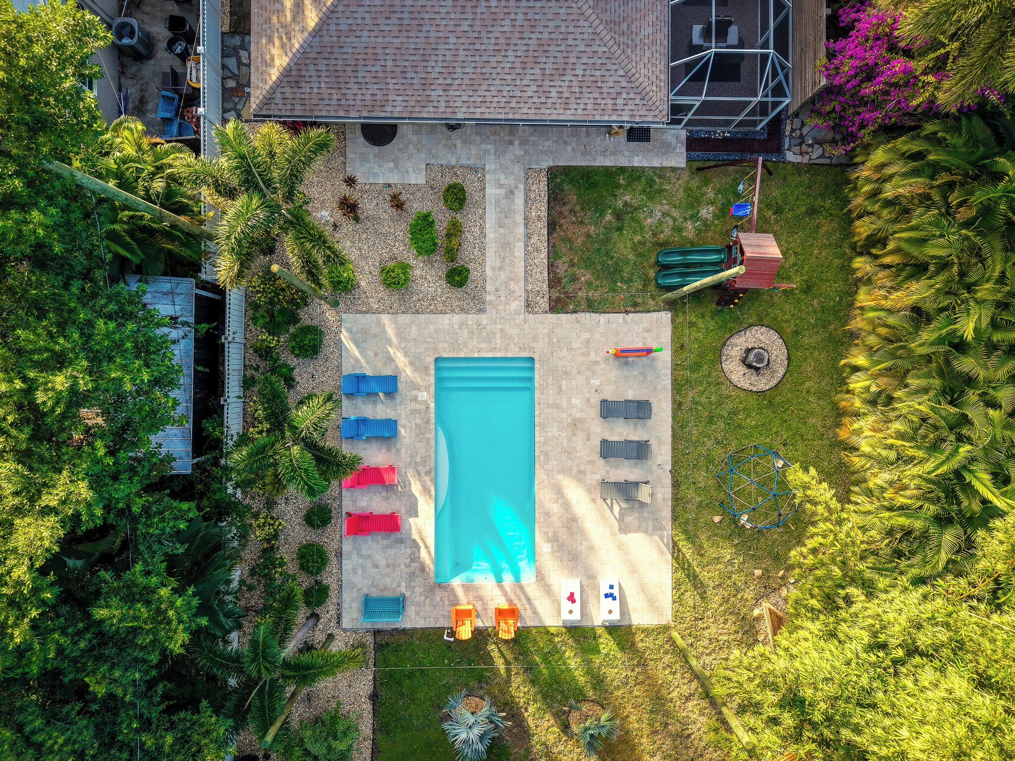 An aerial view of a backyard with a swimming pool, surrounded by greenery and outdoor furniture.