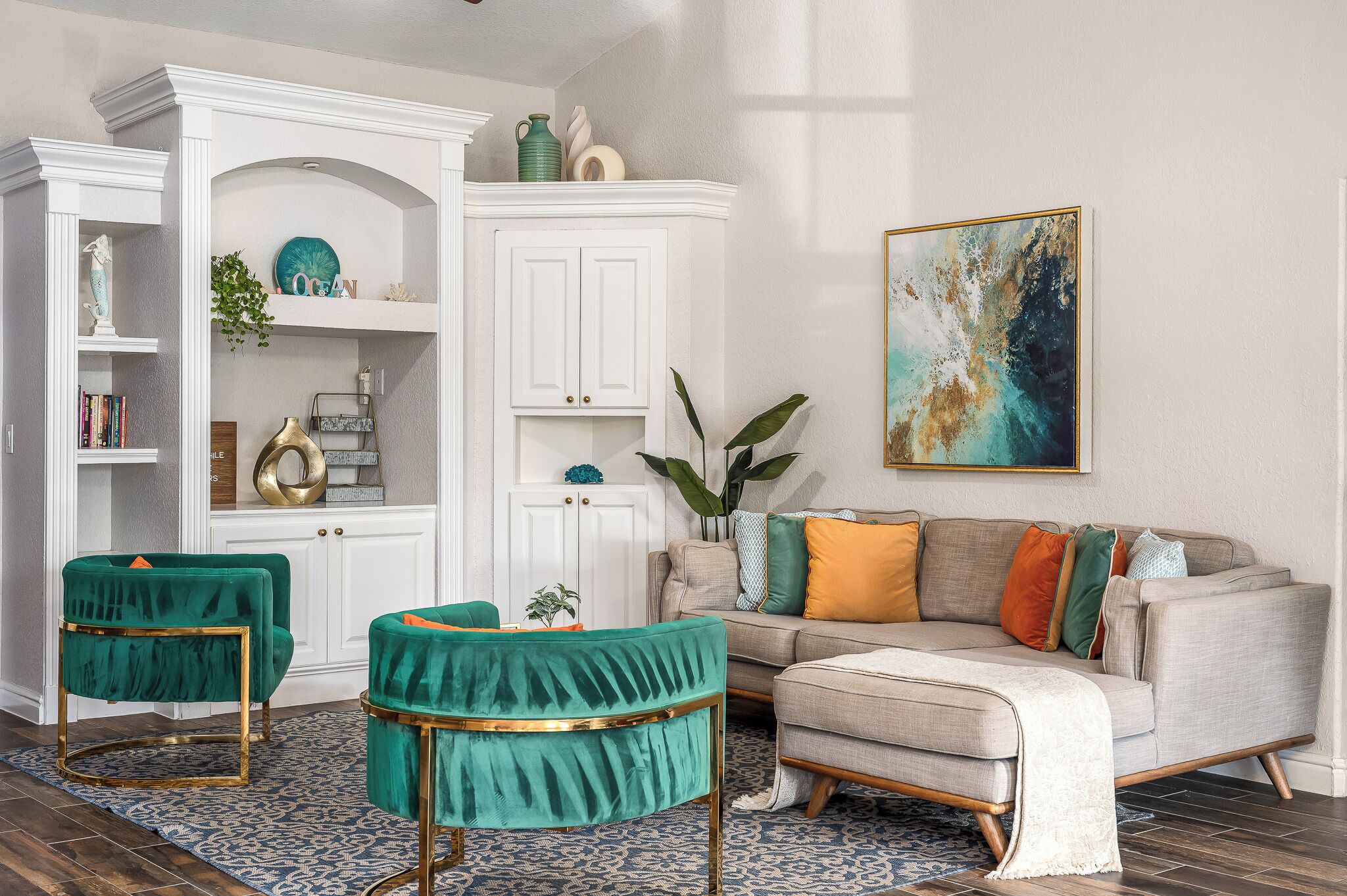 A living room with a beige sofa, teal armchairs, and a white cabinet with decorative items.
