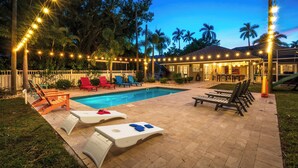 A pool area with lounge chairs, a pool, and string lights. - Near Downtown &Beach! Games! Private Pool! Hot Tub (Bradenton)