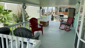 A covered porch with a white railing, red chairs, and a table. - 1B/1B Cottage in Long Island Village Near Space X
 (Port Isabel)