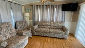 A living room with two patterned sofas, a wooden floor, a ceiling fan, and a 'WELCOME' sign. - 1B/1B Cottage in Long Island Village Near Space X
 (Port Isabel)
