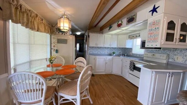 A kitchen with white cabinets, a wooden ceiling, and a dining area with wicker chairs and a glass table. - 1B/1B Cottage in Long Island Village Near Space X
 (Port Isabel)