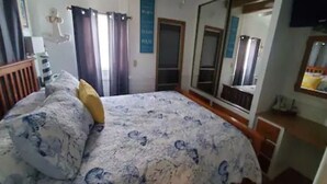 A bedroom with a bed, curtains, a mirror, and a window. - 1B/1B Cottage in Long Island Village Near Space X
 (Port Isabel)