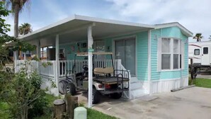 A single-story mobile home with a porch, a small vehicle parked in front, and a trailer in the background. - 1B/1B Cottage in Long Island Village Near Space X
 (Port Isabel)