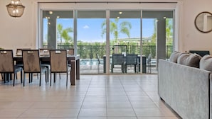 A spacious living area with a dining setup, a large sliding glass door leading to a balcony with a pool view. - Arcades, Pool Table, Craps Table, Huge Galactic Bedroom: Magic Moments (Kissimmee)