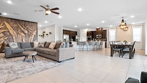 A spacious living room with a grey sofa, a coffee table, and a dining area with a long table and chairs. - Arcades, Pool Table, Craps Table, Huge Galactic Bedroom: Magic Moments (Kissimmee)