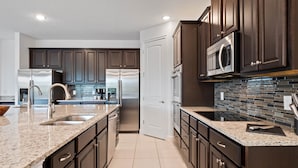 A modern kitchen with dark wood cabinets, stainless steel appliances, and a tiled backsplash. - Arcades, Pool Table, Craps Table, Huge Galactic Bedroom: Magic Moments (Kissimmee)