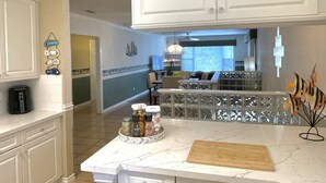 A kitchen with white cabinets, a marble countertop, and a dining area with a table and chairs. - Heated Pool & Hot Tub!  Fall and Winter SPECIAL! (South Padre Island)