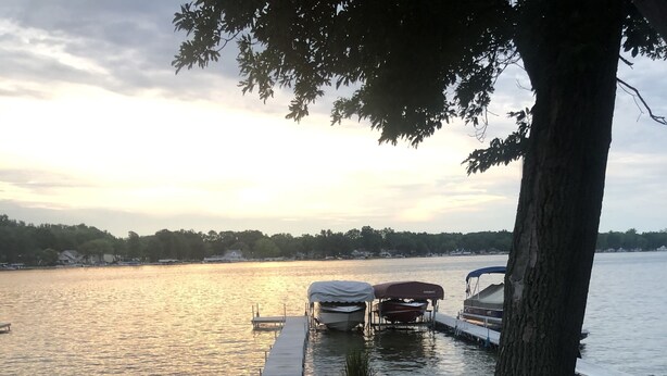 A deck with white railings overlooking a calm lake at sunset.
