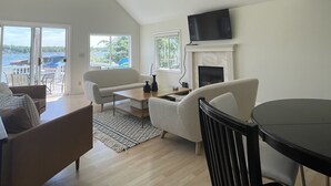 A spacious living area with a high ceiling, a fireplace, a television, and a view of the outdoors.