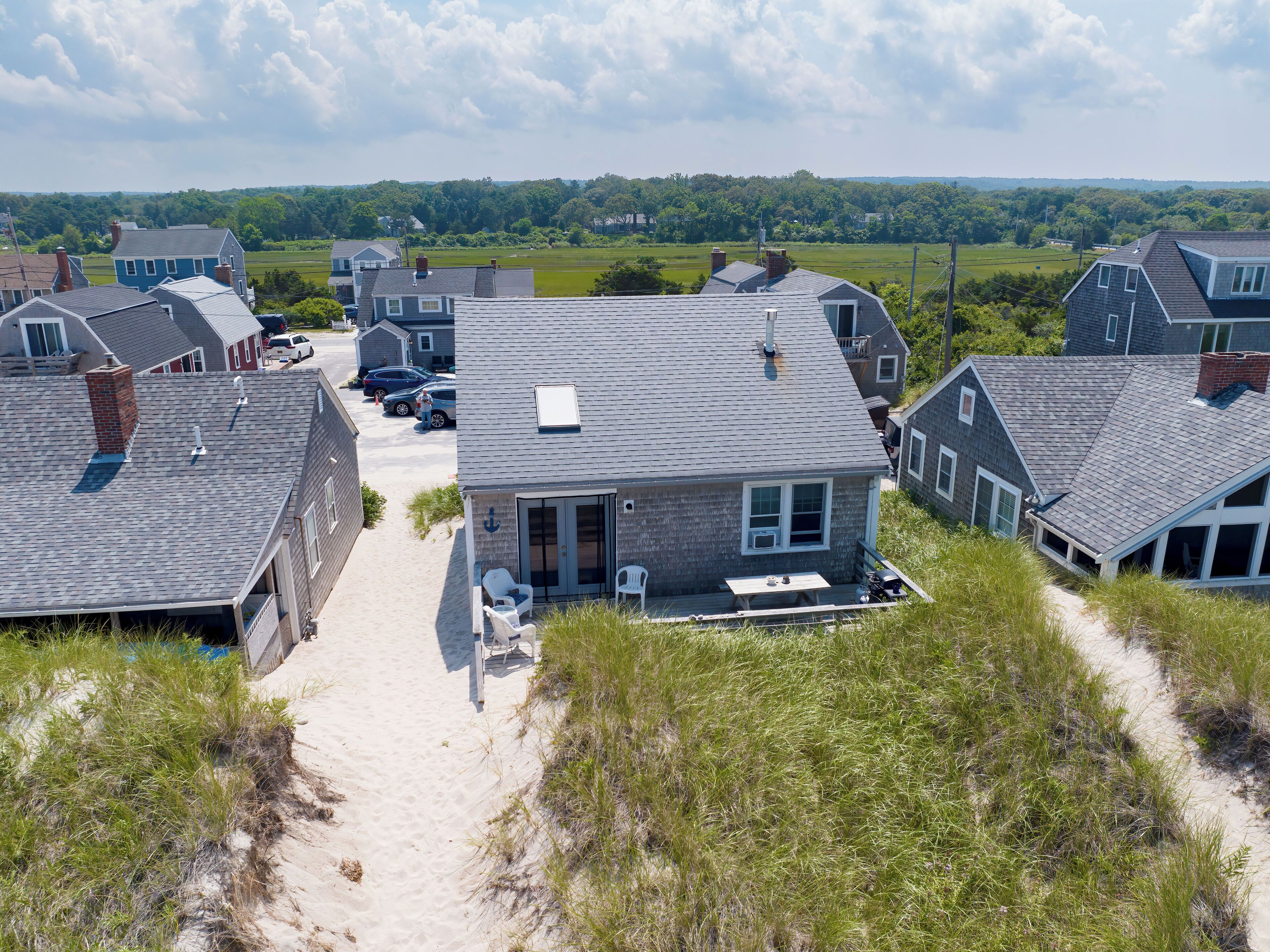 A residential area with multiple houses, a sandy path, and a grassy field.