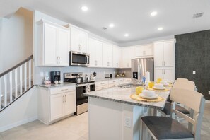 A modern kitchen with white cabinetry, stainless steel appliances, and a central island with seating. - Pool Oasis: 5BR Townhome w Game Room Fun (Kissimmee)