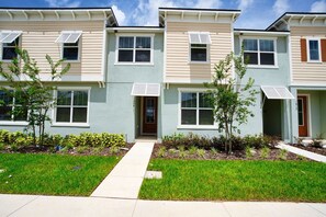A row of townhouses with a central entrance, small front yards, and a clear sky. - Pool Oasis: 5BR Townhome w Game Room Fun (Kissimmee)