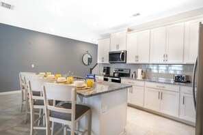 A modern kitchen with white cabinets, a central island, and a dining area with chairs. - Pool Oasis: 5BR Townhome w Game Room Fun (Kissimmee)