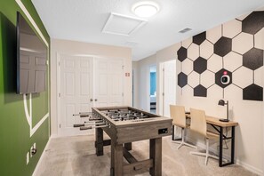 A room with a foosball table, a desk with chairs, and a wall-mounted security camera. - Pool Oasis: 5BR Townhome w Game Room Fun (Kissimmee)