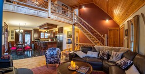 A spacious living area with a high ceiling, a staircase, a kitchen, and a dining area. - Pet-Friendly Adirondack Retreat | Hot Tub, Fire Pit near Whiteface Mountain (Jay)