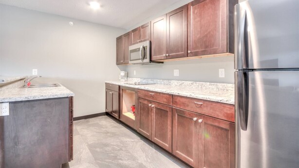 A kitchen with wooden cabinets, a stainless steel refrigerator, and a microwave. - Suite 218 - 1BR Apartment, King Bed, Kitchen, 2nd (Rapid City)