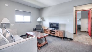 A living room with a sofa, coffee table, TV, and lamp. - Suite 218 - 1BR Apartment, King Bed, Kitchen, 2nd (Rapid City)