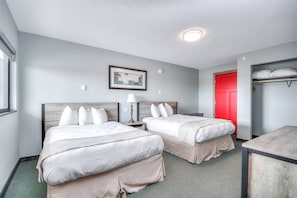 A hotel room with two beds, a red door, a framed picture on the wall, and a lamp on the nightstand.