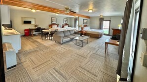 A hotel room with a kitchenette, a dining area, a sofa, a bed, and a ceiling fan.