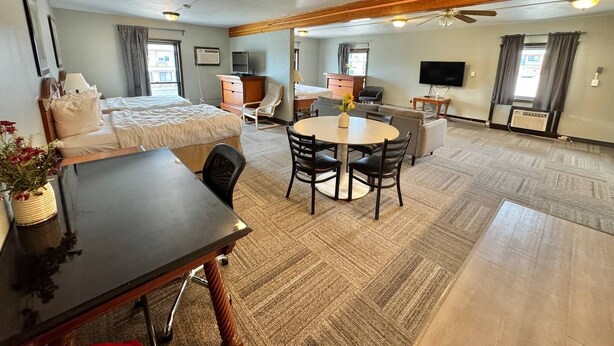 A hotel room with a bed, a desk, a dining table, a TV, and a ceiling fan.
