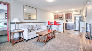 A modern living room with a sofa, coffee table, and red chairs, a kitchen with cabinets and appliances, and a large mirror on the wall.