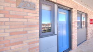 A brick building with a blue door and a window, a number sign '204' above the door, and a red mailbox on the right.