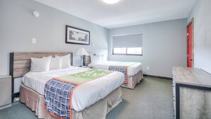 A hotel room with two beds, a desk, a lamp, a framed picture, and a window.