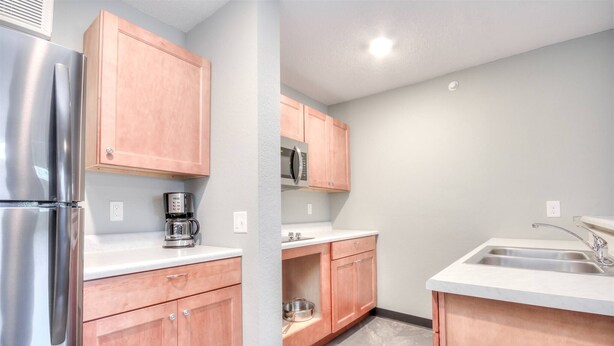 A kitchen with wooden cabinets, a stainless steel refrigerator, a microwave, a coffee maker, and a sink.