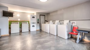 A laundry room with multiple washing machines, a television, and a red chair.