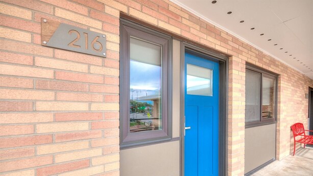 A building with a blue door, a number plate with '216', and a red chair outside.