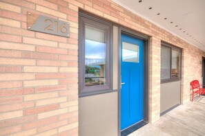 A building with a blue door, a number plate with '216', and a red chair outside.