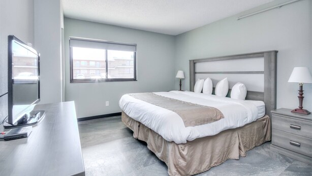 A modern hotel room with a large bed, a desk, a TV, and a window with a city view.