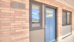 A brick building with a blue door and a window, and a house number sign.