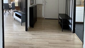 A hallway with a wooden floor, a door, a bench, and a TV stand.