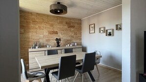 A modern dining area with a wooden table and chairs, a stone accent wall, and a hanging light fixture.