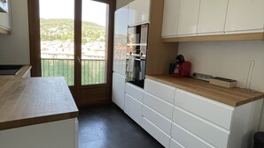 A modern kitchen with white cabinets, a wooden countertop, and a view of a hillside through a sliding glass door.