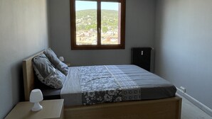 A bedroom with a bed, a nightstand, a radiator, and a window with a view of a hilly landscape.