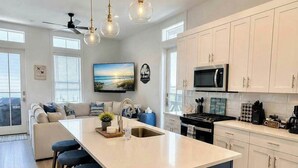 Une cuisine moderne dotée d’un îlot central, de tabourets de bar, d’un ventilateur de plafond et d’une grande fenêtre.