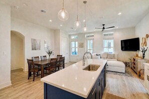 A modern kitchen with a central island, dining area, and a living space with a sofa and TV.